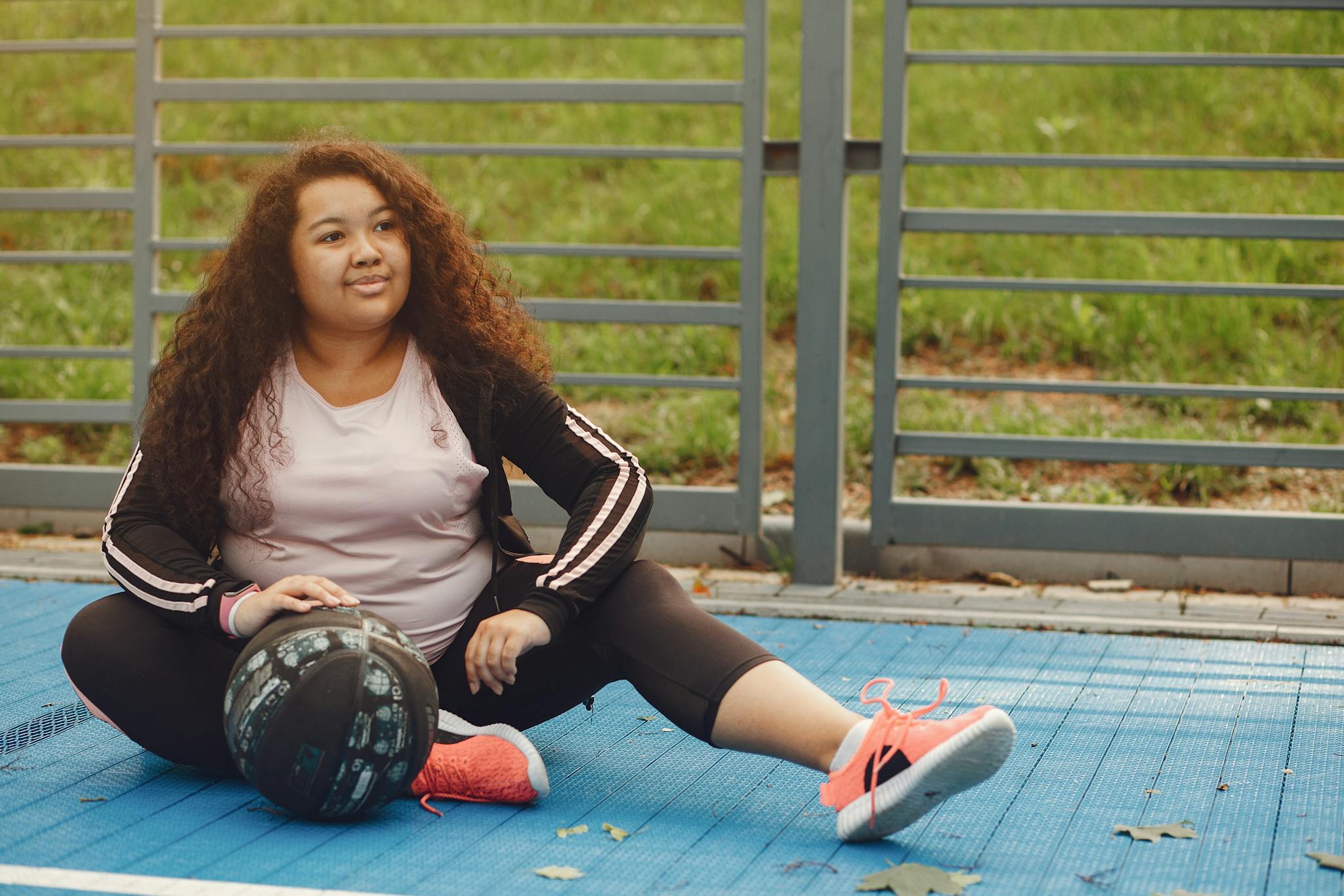 A woman enjoys a moment of relaxation sitting on an outdoor basketball court with a ball.