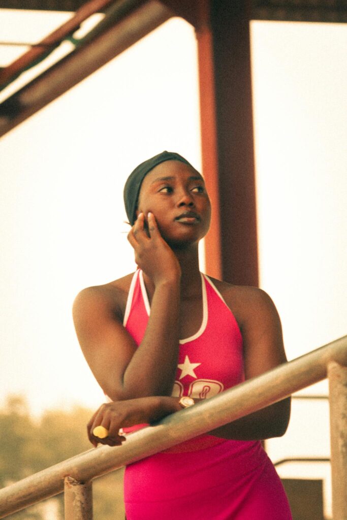 A young female athlete in red sportswear leans on a railing, reflecting at a sports facility.